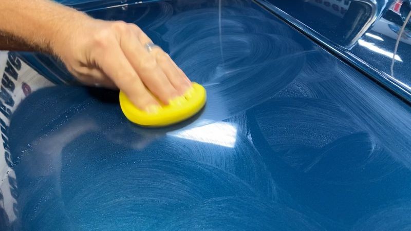 Action shot of applying paint coating onto wet surface of vehicle.
